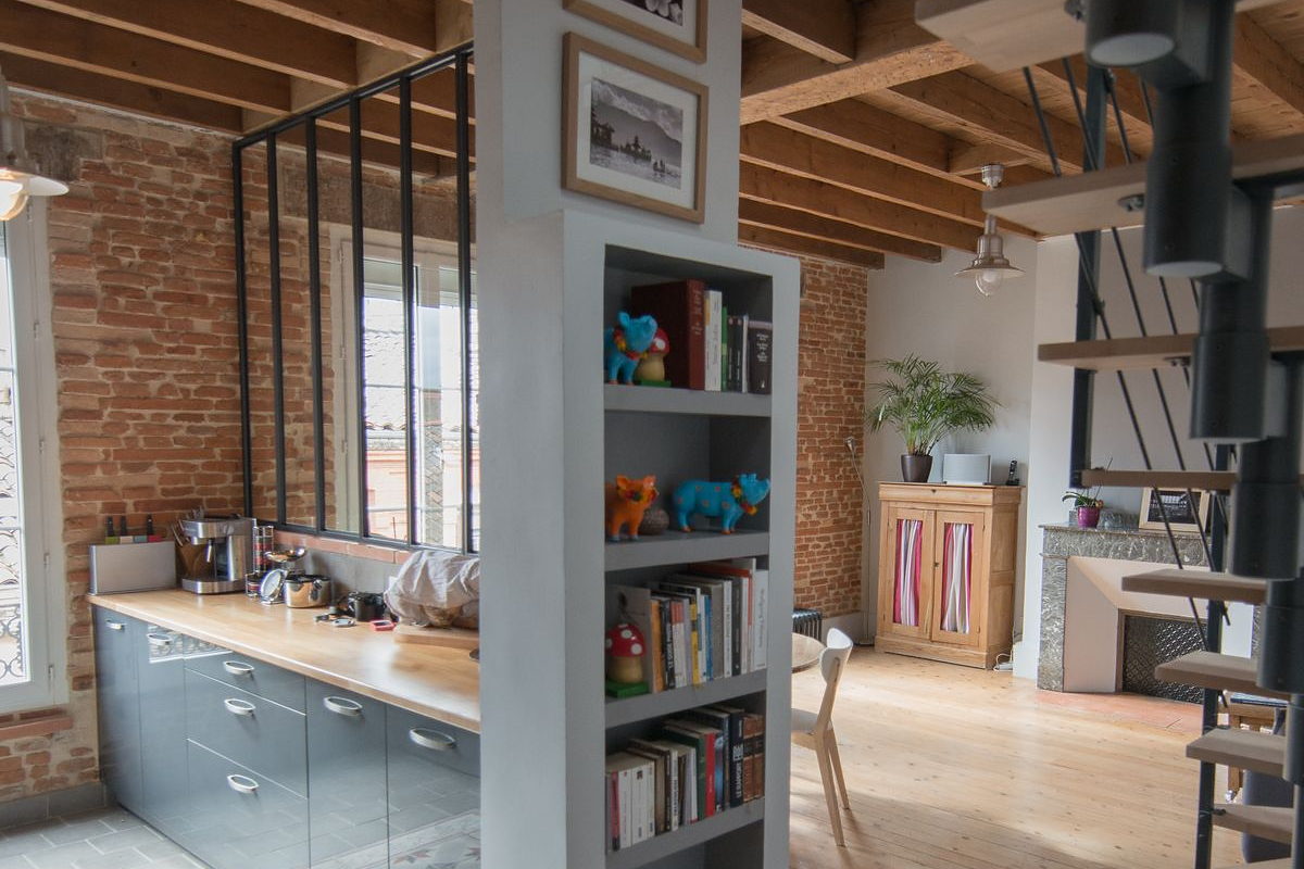 Séjour d’un appartement toulousain remis au propre : mur de brique, verrière, parquet et poutres apparentes